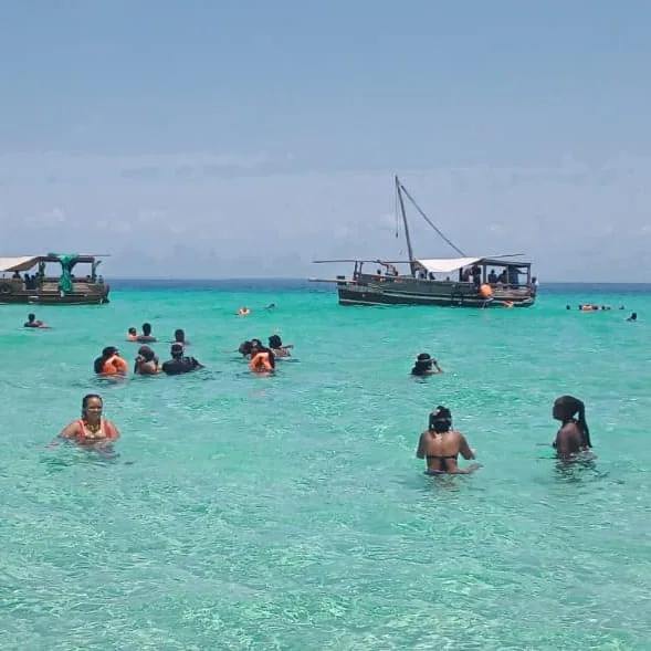 Guests swimming beside a boat on a turquoise sandbank on the Kenyan coast